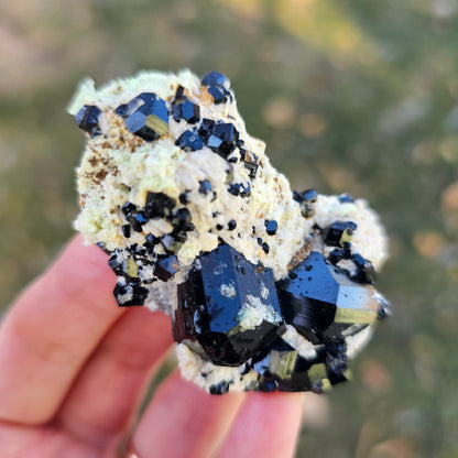 Mineral specimen held in a hand with a blurred natural background