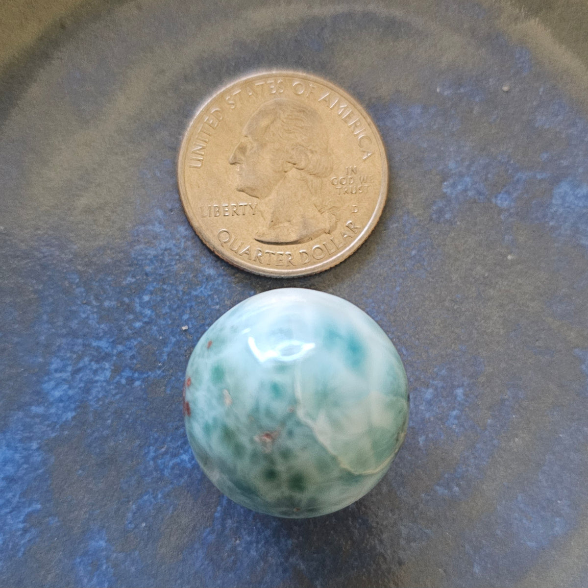 Grade AA natural blue Larimar sphere 16.8g 0.75 inch held in hand showing ocean wave patterns and natural hematite spots