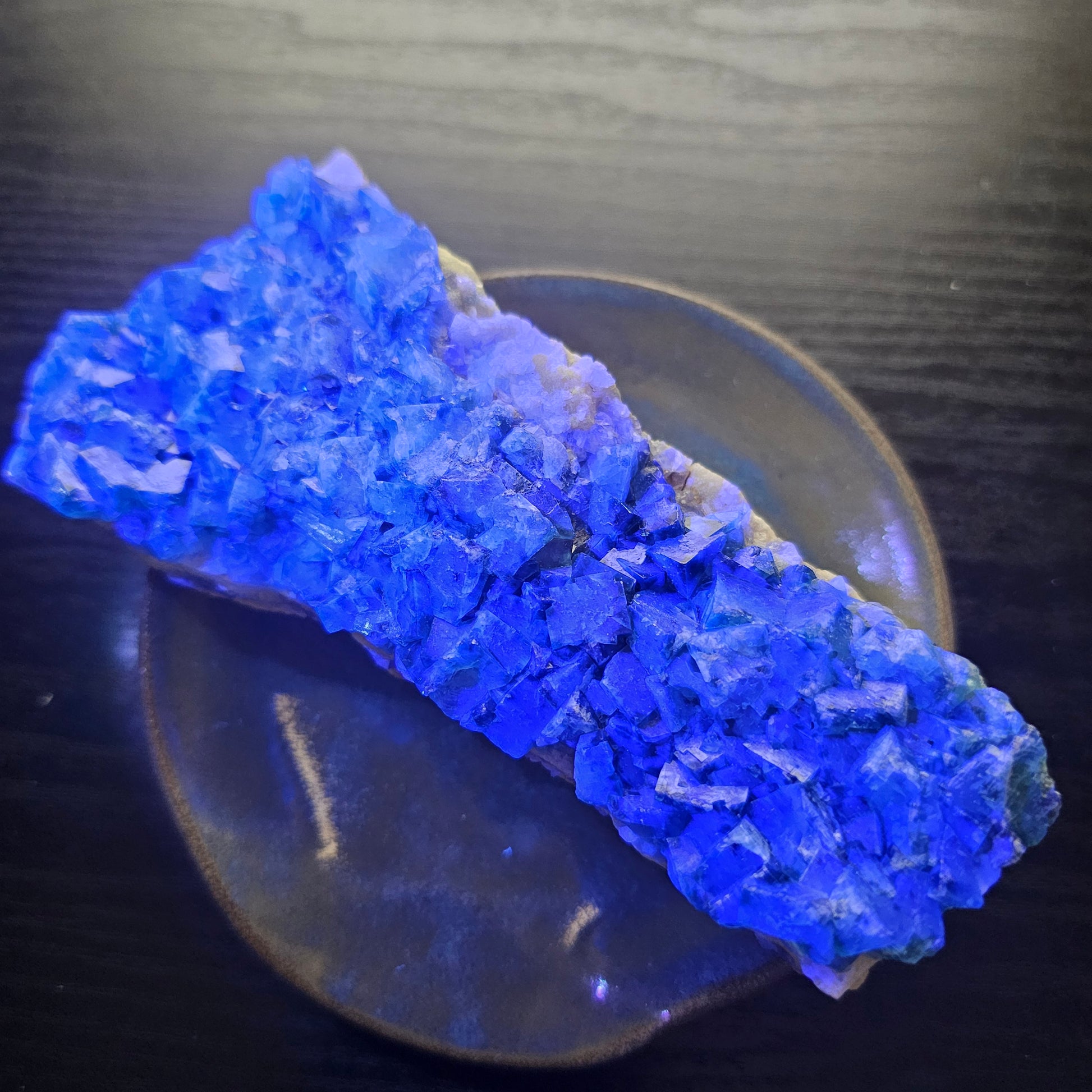 A 425g Madagascar Green Fluorite cube cluster displaying a vibrant, deep blue-purple fluorescence color change under a long-wave UV light source.