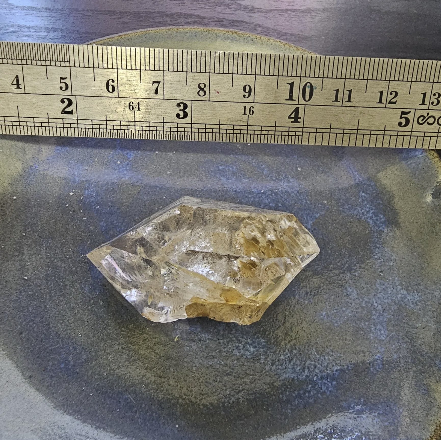 A hand holding a 1 7/8 inch genuine Herkimer Diamond crystal from New York, showcasing its raw size, clear transparency, and unique trigonal structure.