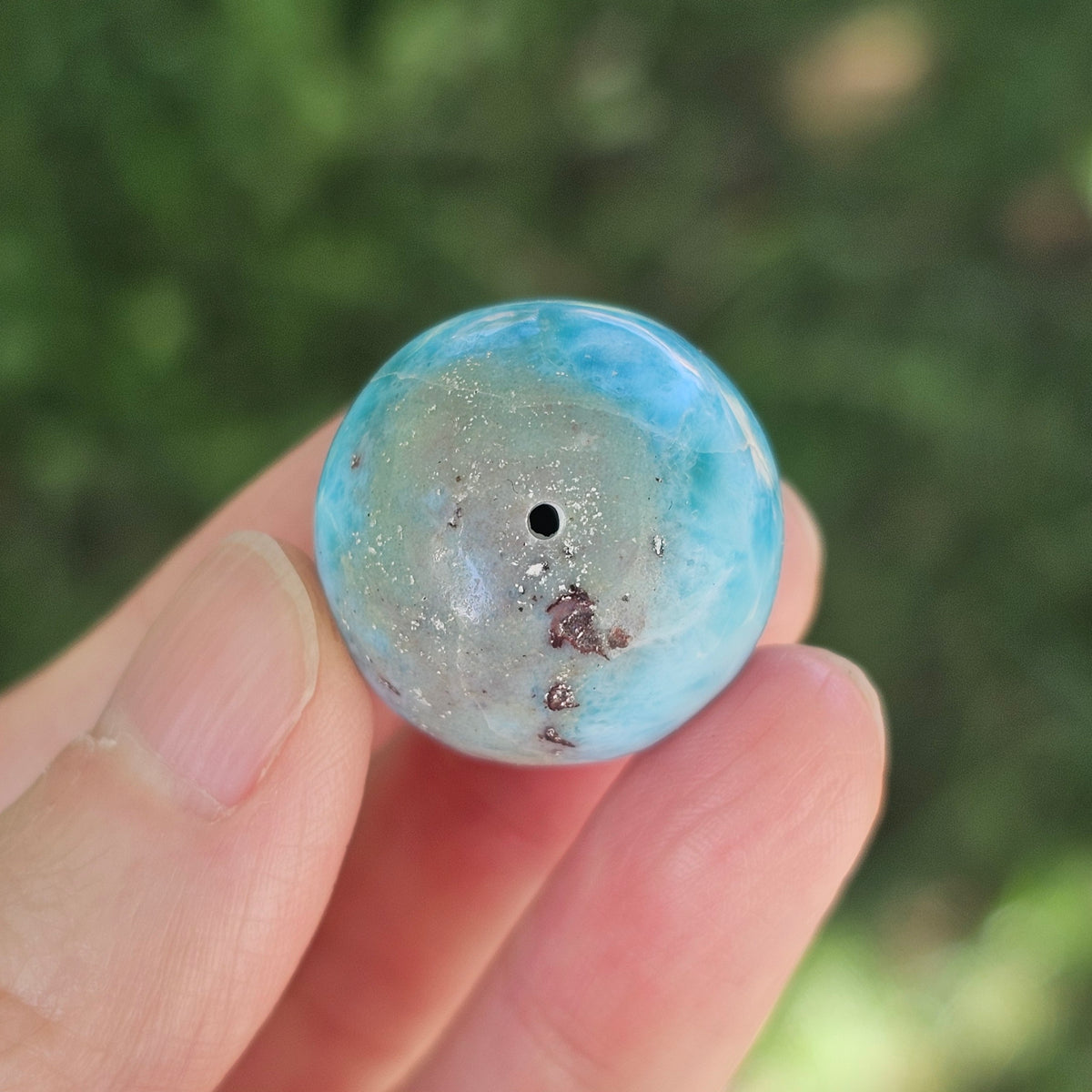 Close-up view of the single half-drilled hole on the surface of a polished Larimar gemstone sphere.