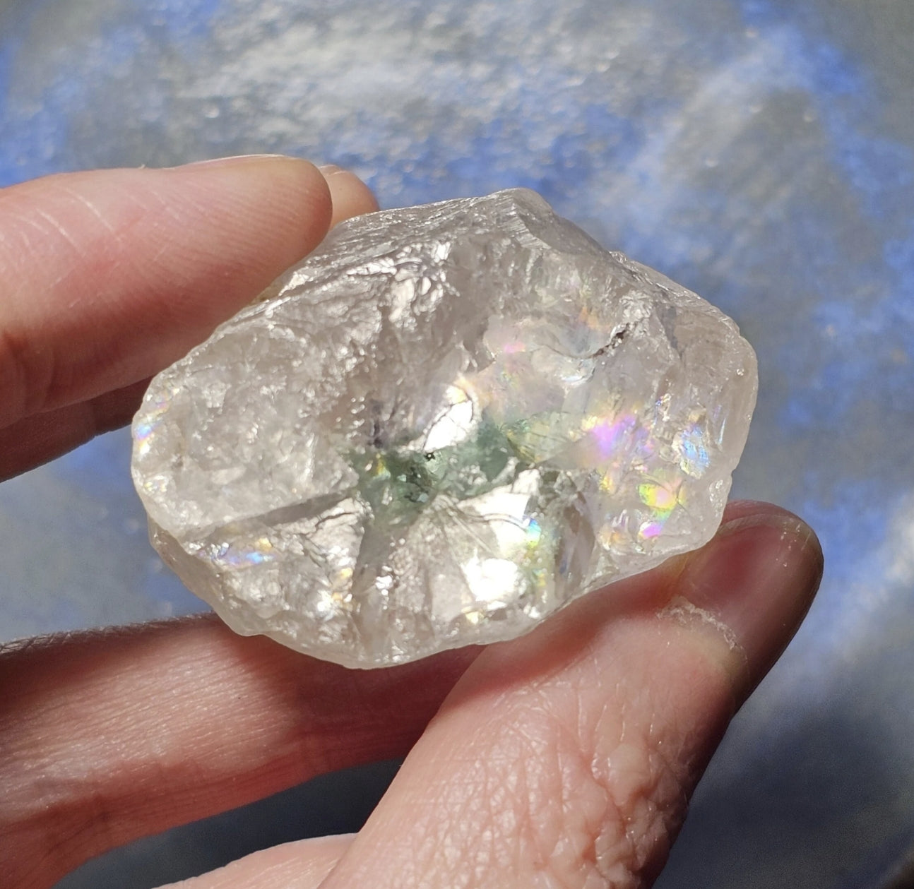 Raw diamond held in a hand against a blue background