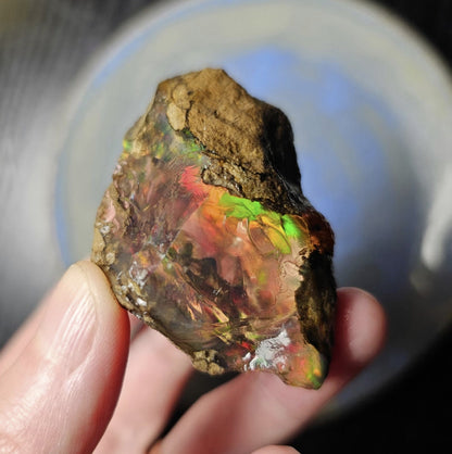 Multicolored opal stone held in a hand with a blurred background