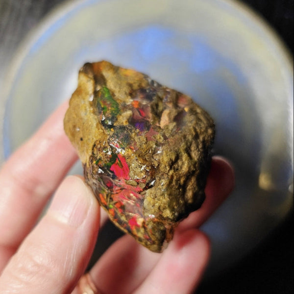 Hand holding a colorful mineral specimen against a reflective surface