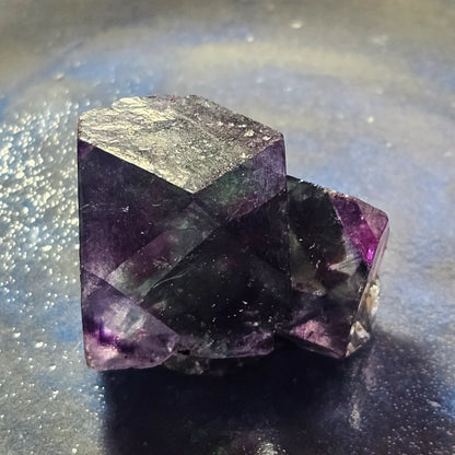 Close-up of an Alien Eye Fluorite specimen from Erongo, Namibia, showing a 1.5 inch twin crystal with deep green and purple aurora-like phantom zones.