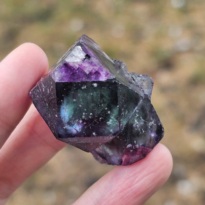 Close-up of an Alien Eye Fluorite specimen from Erongo, Namibia, showing a 1.5 inch twin crystal with deep green and purple aurora-like phantom zones.