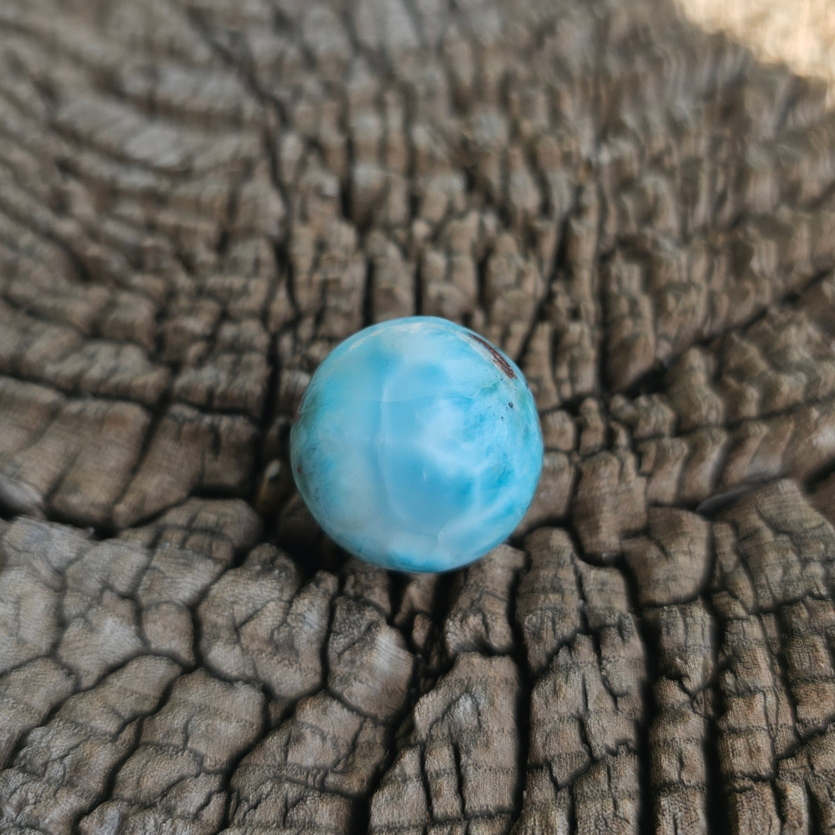 Grade AA natural blue Larimar sphere 16.8g 0.75 inch held in hand showing ocean wave patterns and natural hematite spots