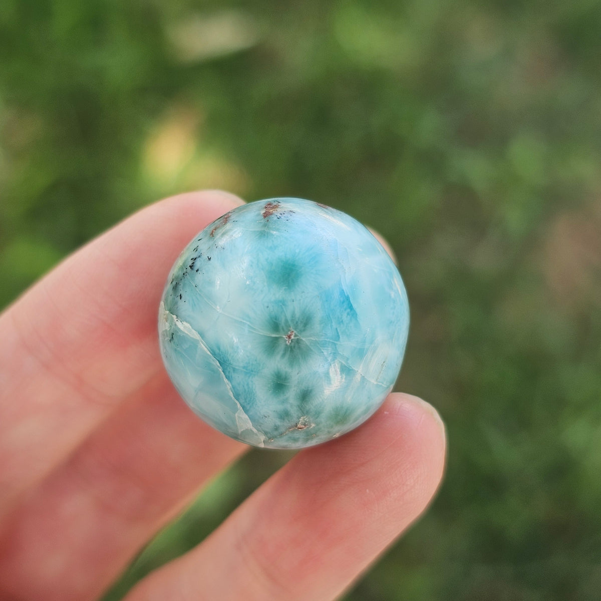 Grade AA natural blue Larimar sphere 16.8g 0.75 inch held in hand showing ocean wave patterns and natural hematite spots