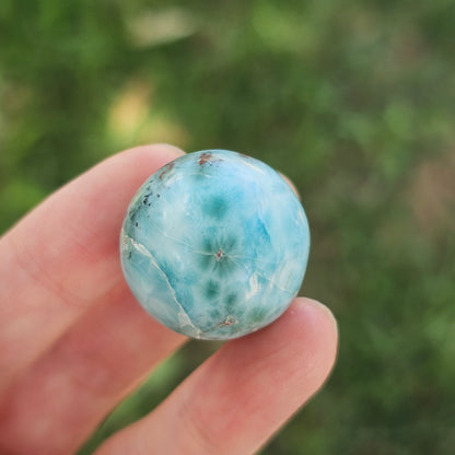 Grade AA natural blue Larimar sphere 16.8g 0.75 inch held in hand showing ocean wave patterns and natural hematite spots