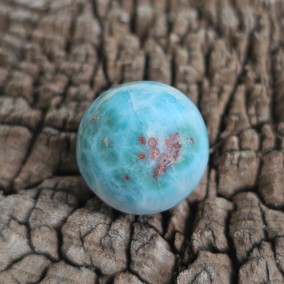 Grade AA natural blue Larimar sphere 16.8g 0.75 inch held in hand showing ocean wave patterns and natural hematite spots