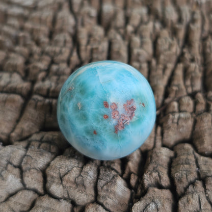 Grade AA natural blue Larimar sphere 16.8g 0.75 inch held in hand showing ocean wave patterns and natural hematite spots