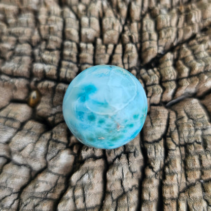 Grade AA natural blue Larimar sphere 16.8g 0.75 inch held in hand showing ocean wave patterns and natural hematite spots