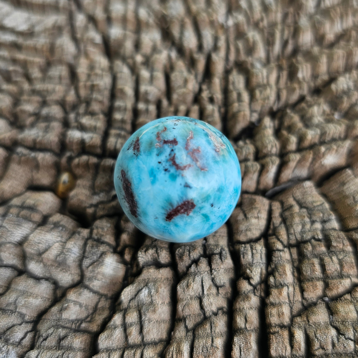 Grade AA natural blue Larimar sphere 16.8g 0.75 inch held in hand showing ocean wave patterns and natural hematite spots
