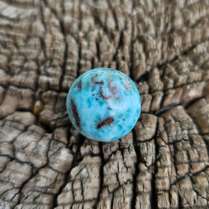 Grade AA natural blue Larimar sphere 16.8g 0.75 inch held in hand showing ocean wave patterns and natural hematite spots