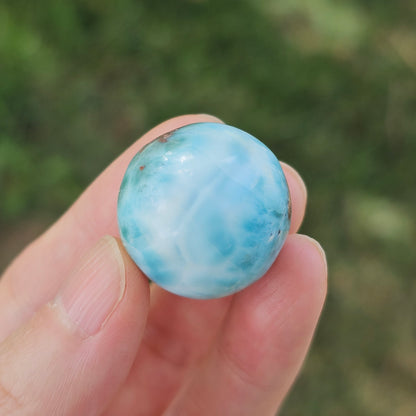 Grade AA natural blue Larimar sphere 16.8g 0.75 inch held in hand showing ocean wave patterns and natural hematite spots