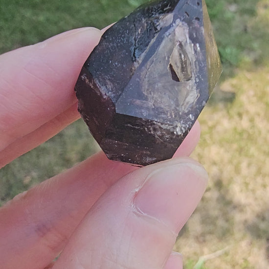 A close-up video of a hand rotating an 18g Brandberg amethyst crystal point in natural daylight, revealing its deep purple internal phantoms, clarity, and reflective facets.