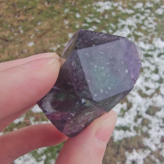 Handheld video rotating a 33.6g Alien Eye Fluorite specimen under a light source to reveal shifting aurora-like green and purple phantom zones within the twin crystal structure.