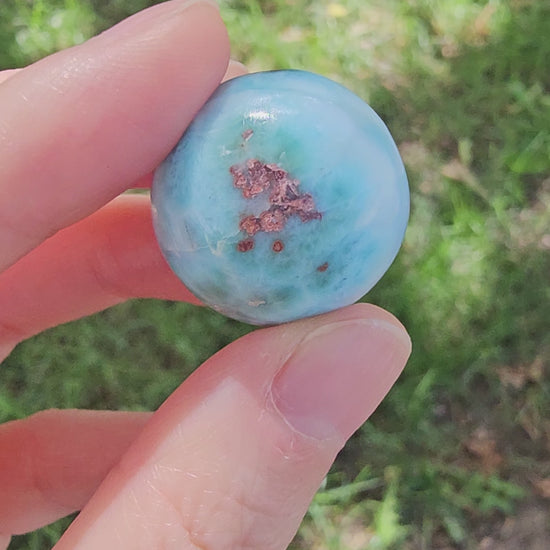 Grade AA natural blue Larimar sphere 16.8g 0.75 inch held in hand showing ocean wave patterns and natural hematite spots