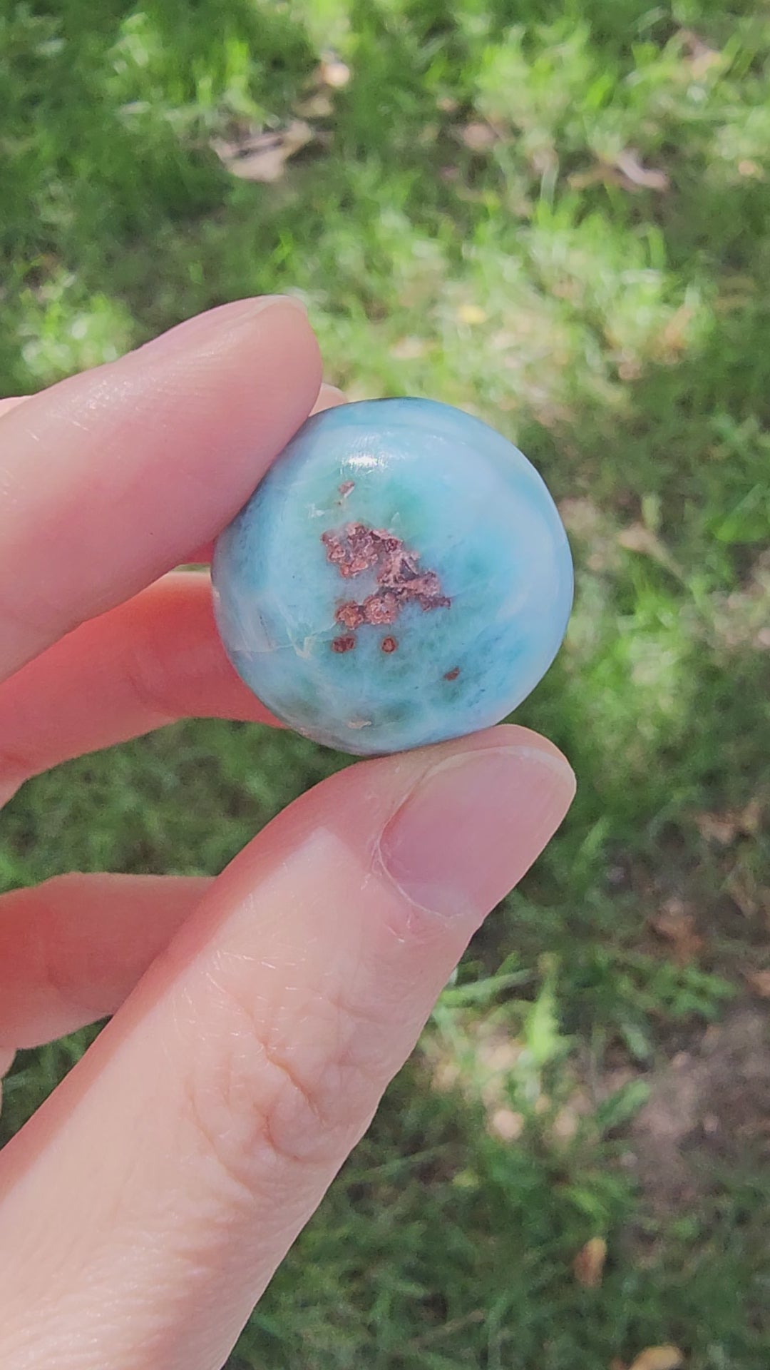 Grade AA natural blue Larimar sphere 16.8g 0.75 inch held in hand showing ocean wave patterns and natural hematite spots