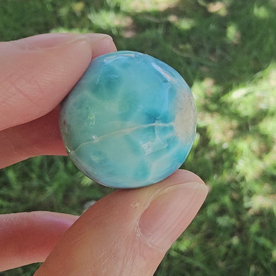 Video showing a hand rotating a 14.2g natural blue Larimar sphere, displaying its ocean-wave marbling, polished surface, and single half-drilled hole.