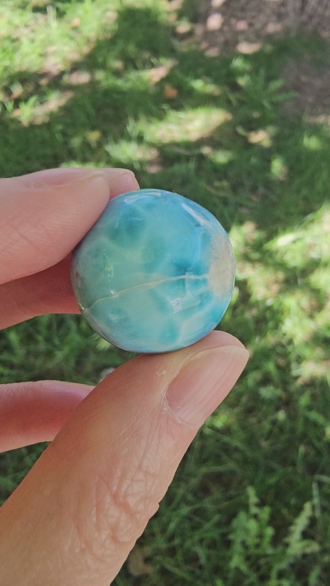 Video showing a hand rotating a 14.2g natural blue Larimar sphere, displaying its ocean-wave marbling, polished surface, and single half-drilled hole.