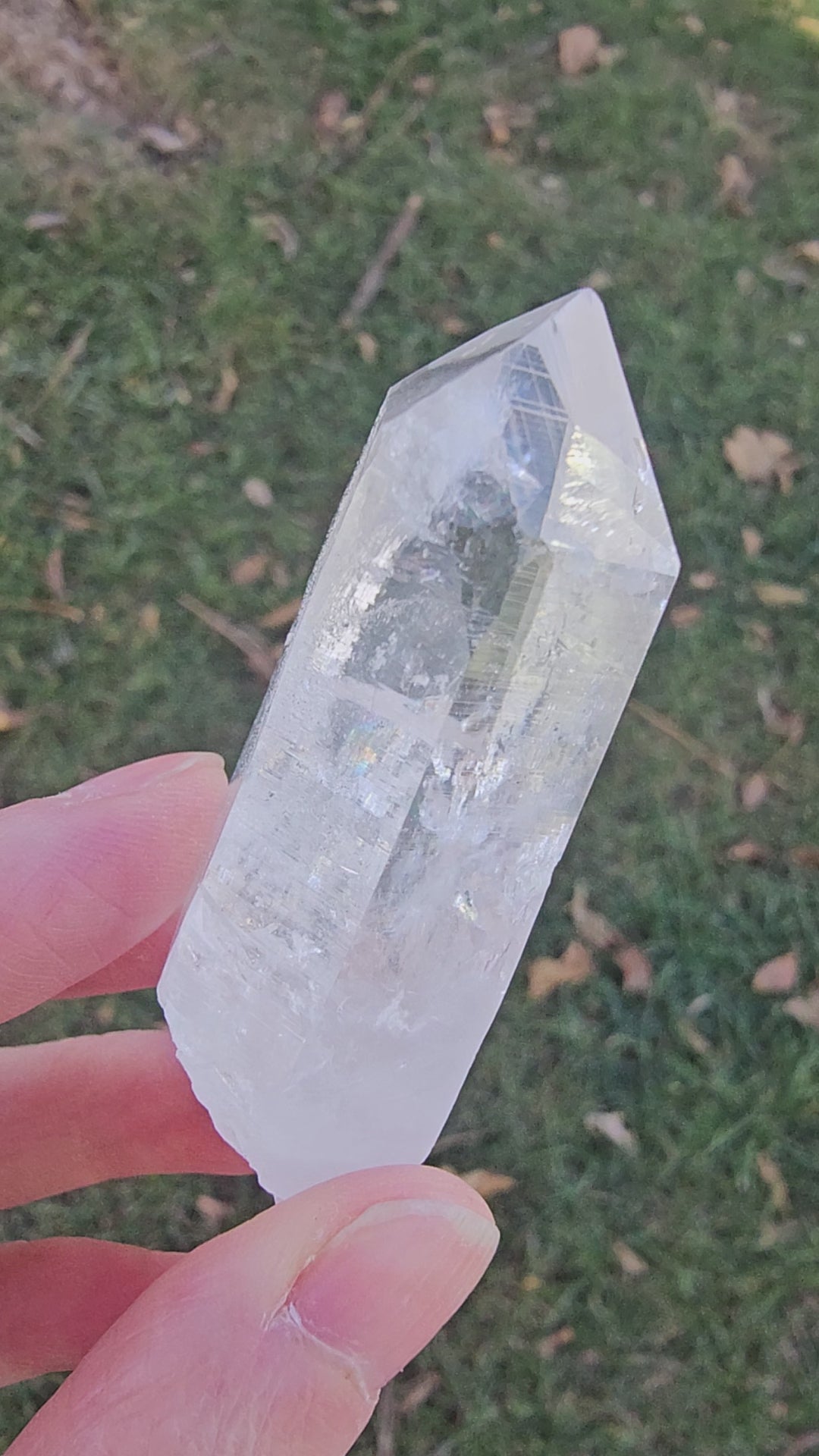 Close-up 360-degree video of a natural Colombian Lemurian Seed Quartz "Blade of Light" crystal. The footage highlights the specimen’s pristine optical clarity, distinct horizontal striations, and vivid internal rainbow flashes as it is rotated under natural light.